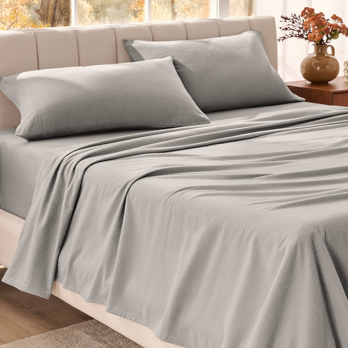 Bed sheets on a neatly made bed in a bright bedroom with large windows.
