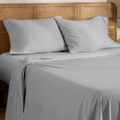 Organic jersey bed sheets and pillows on a bed with a wicker headboard.