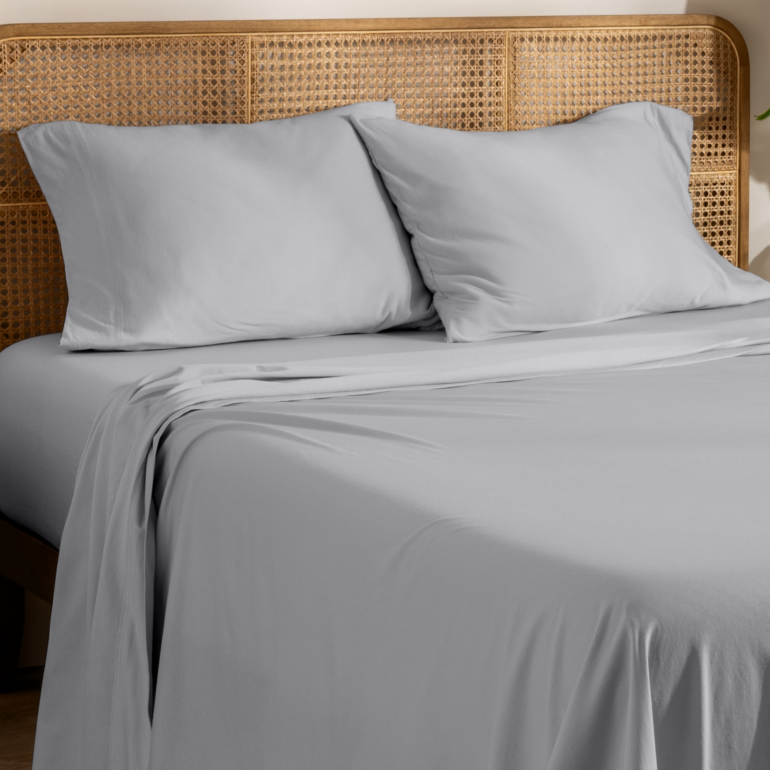 Organic jersey bed sheets and pillows on a bed with a wicker headboard.