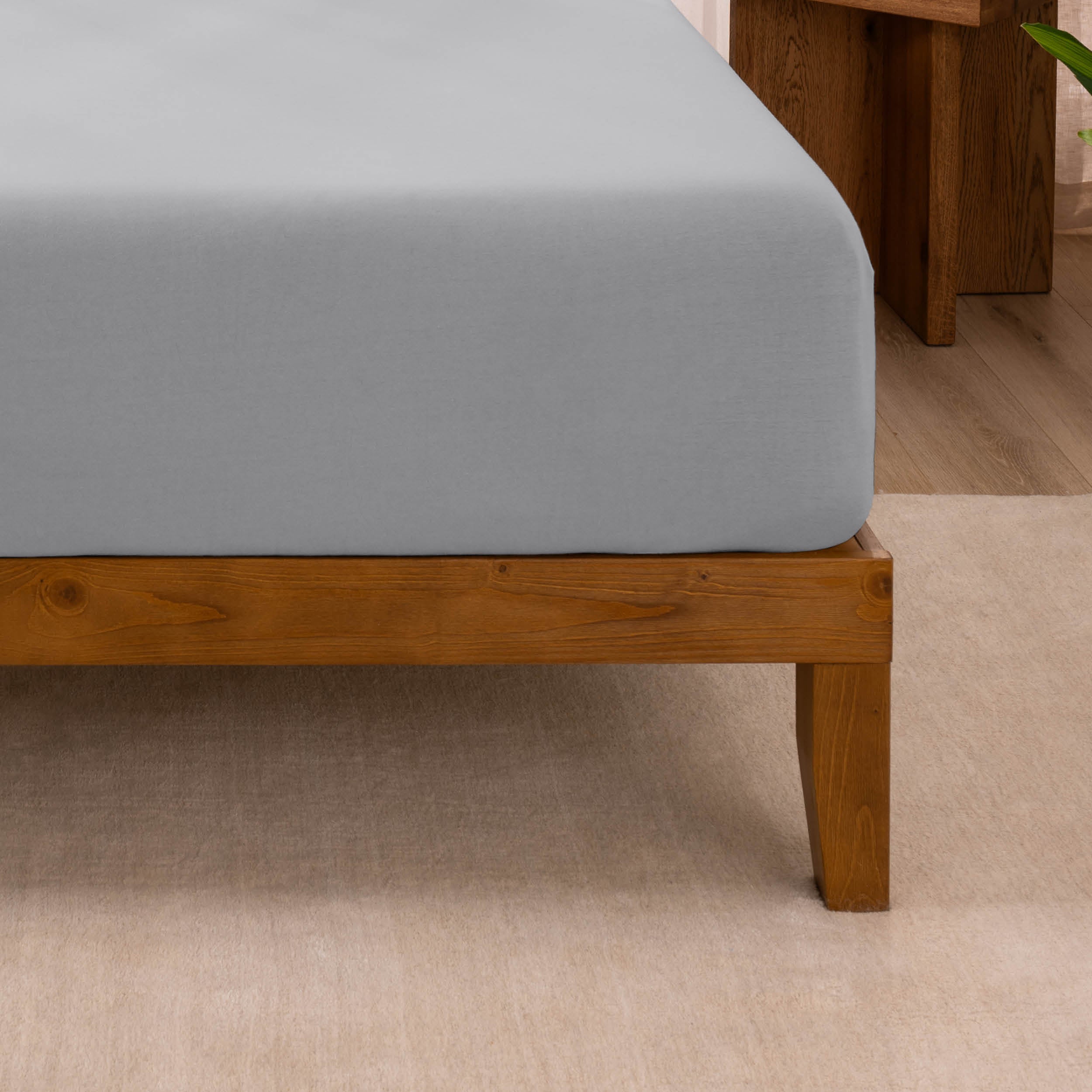 Fitted sheet on a wooden bed frame with a neutral background