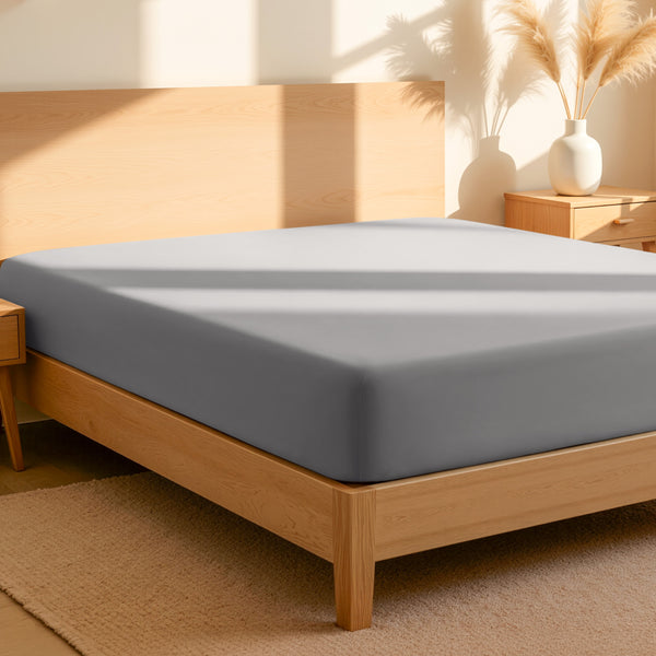 Fitted sheet on a bed in a bedroom setting with a lamp and plant.