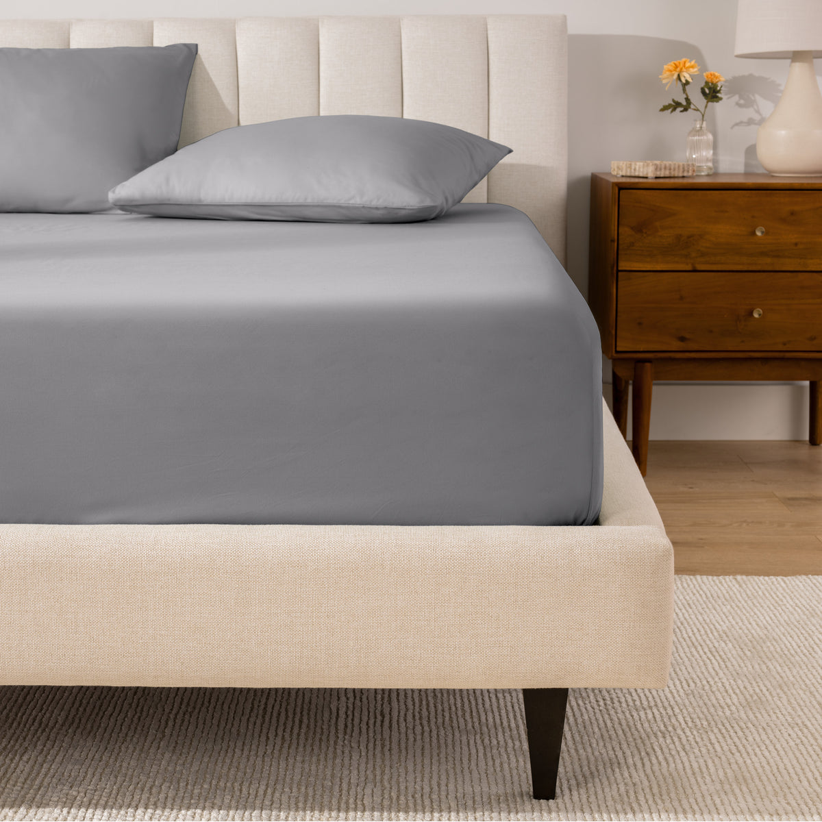 A percale fitted sheet and pillowcases on a bed in a bedroom with a wooden nightstand.