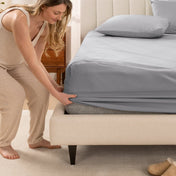 Woman in pajamas adjusting bed sheets on a bed.