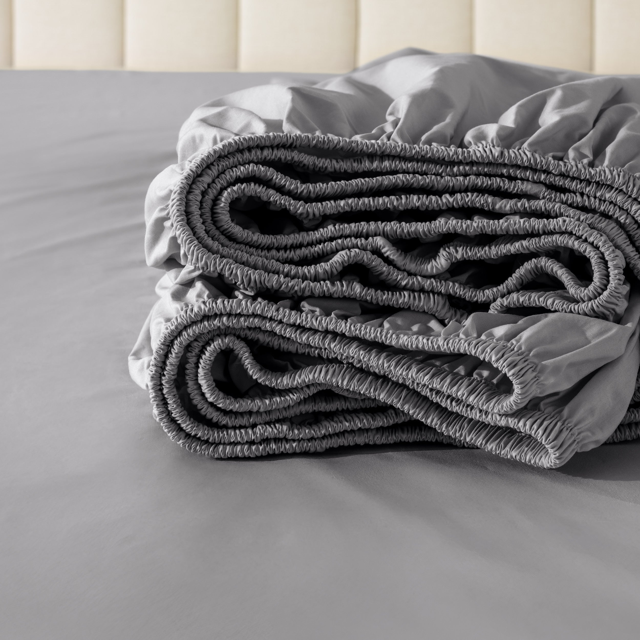 Folded fitted sheet on a bed with a neutral background