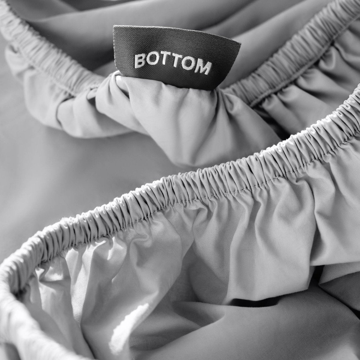 Close-up of a fitted sheet with a black fabric brand label reading BOTTOM.