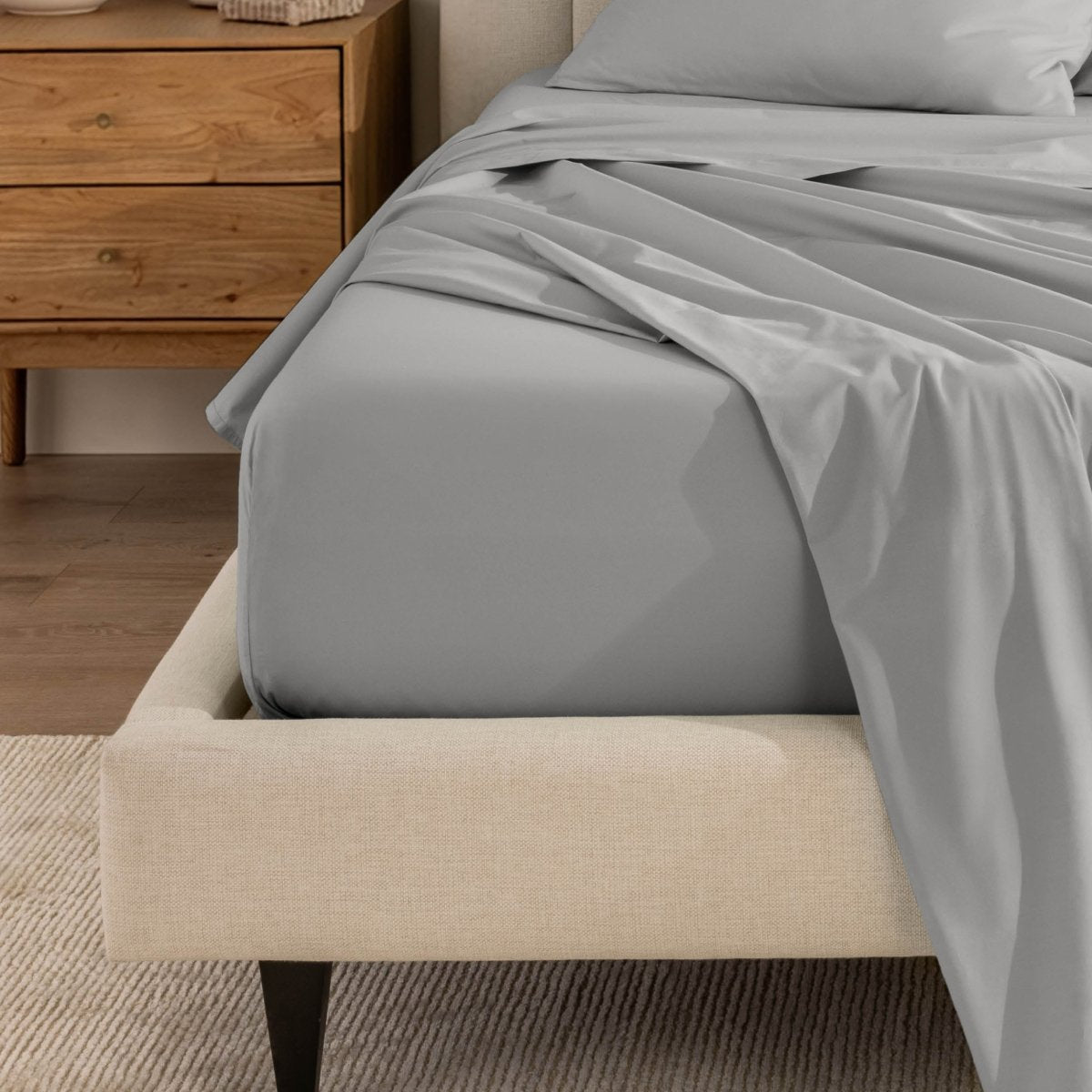 Top sheet and a matching fitted sheet on a bed with a beige bed frame