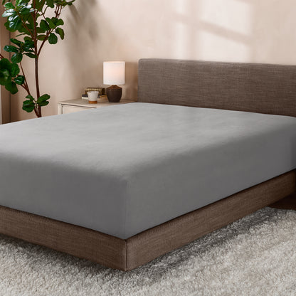 Bed with fitted sheet in a room with a lamp and plant.