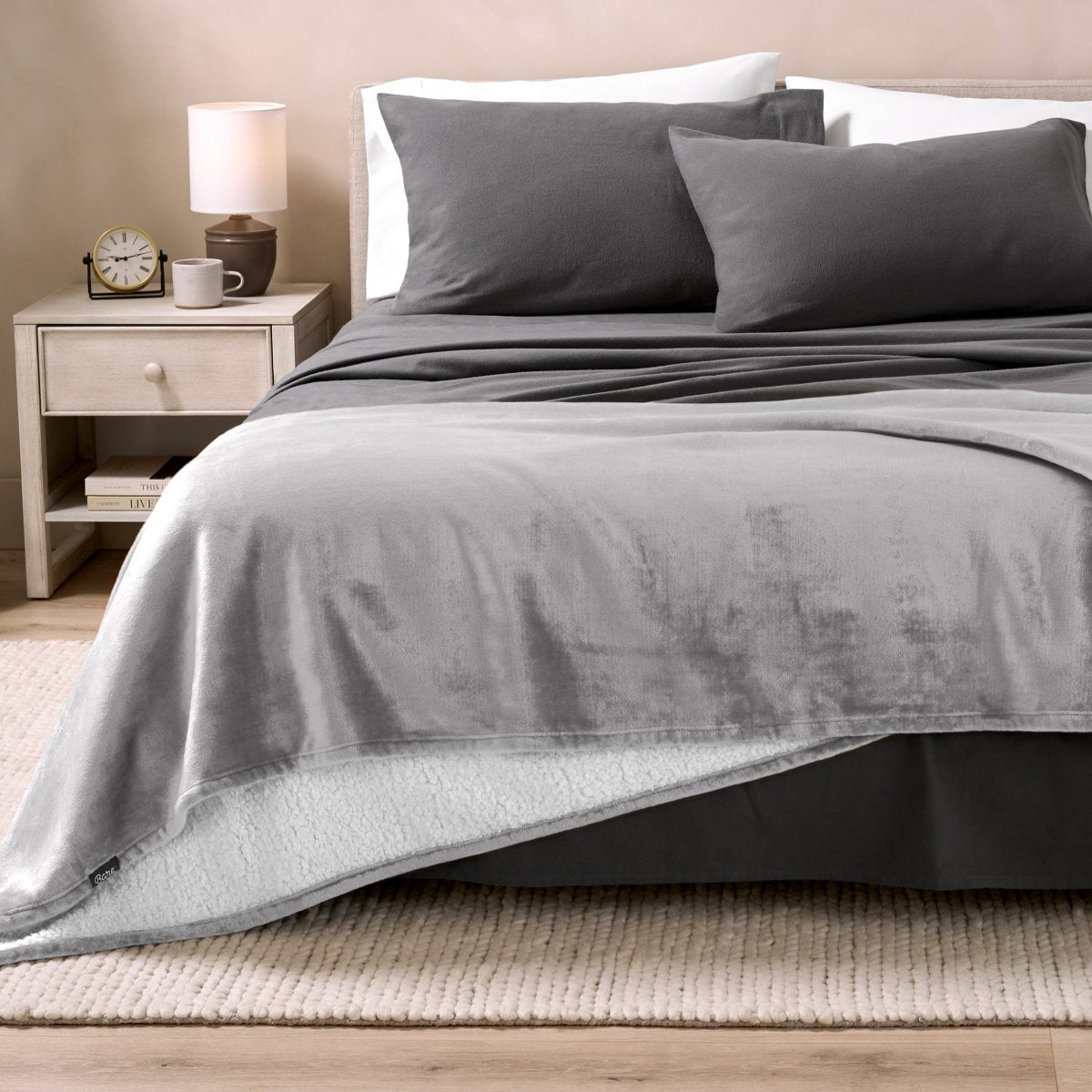 Sherpa blanket on the end of a bed in a bedroom with a nightstand and lamp.