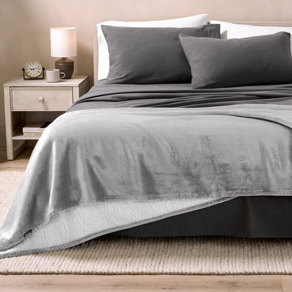 Sherpa blanket on the end of a bed in a bedroom with a nightstand and lamp.