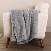 Faux shearling blanket draped over a beige armchair with a wooden base.