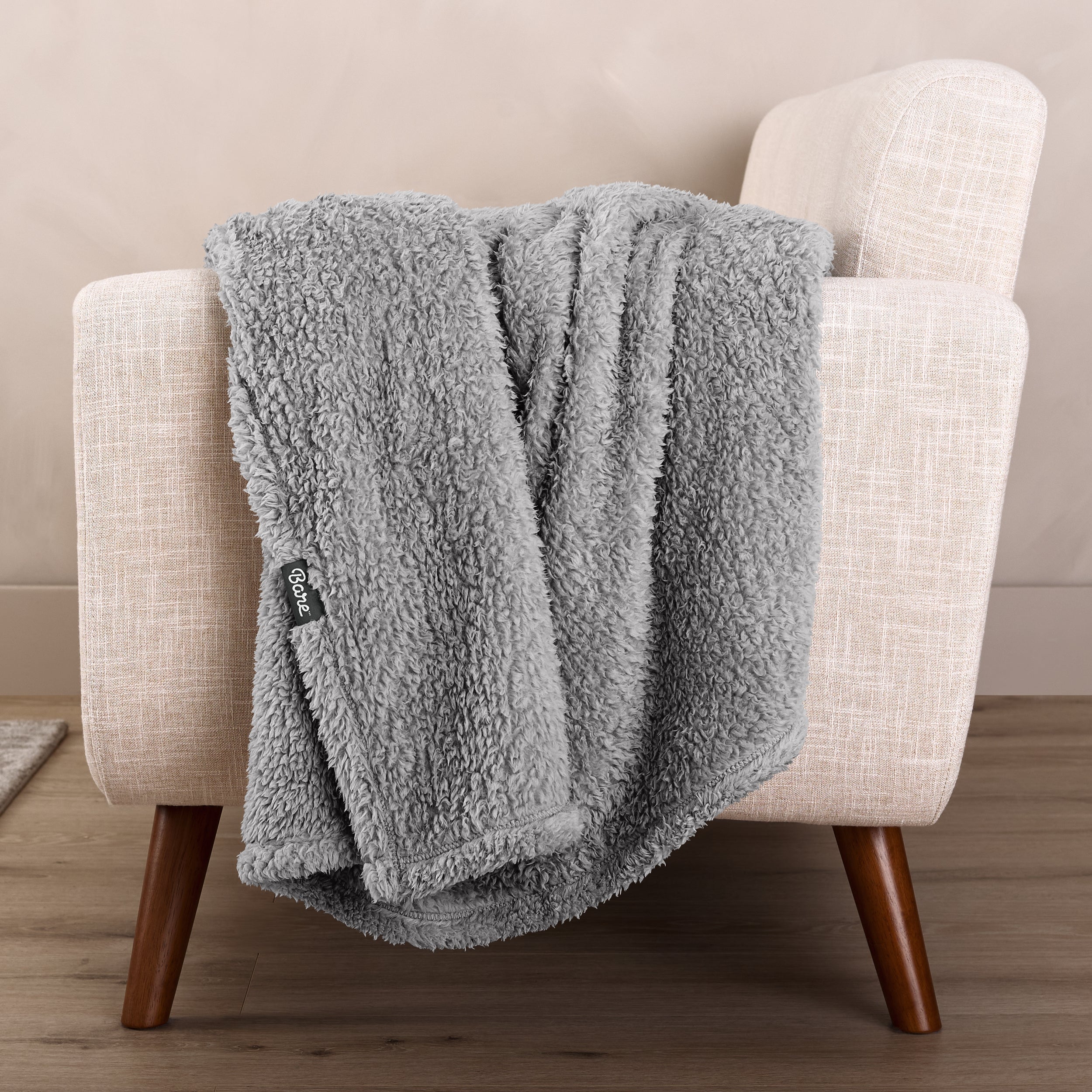 Faux shearling blanket draped over a beige armchair with a wooden base.