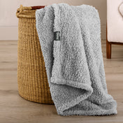 Fluffy blanket draped over a woven basket on a wooden floor.