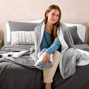 A woman sitting on a bed with a Sherpa blanket around her