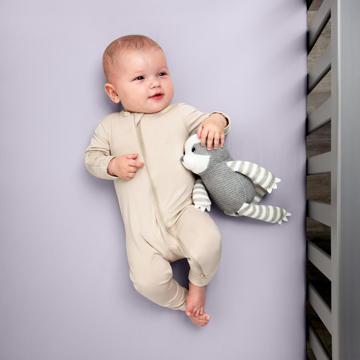 Baby in a beige onesie holding a gray and white striped toy while in a crib