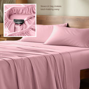 Bed sheets and pillowcases on a bed with a wooden headboard and plants in the background.