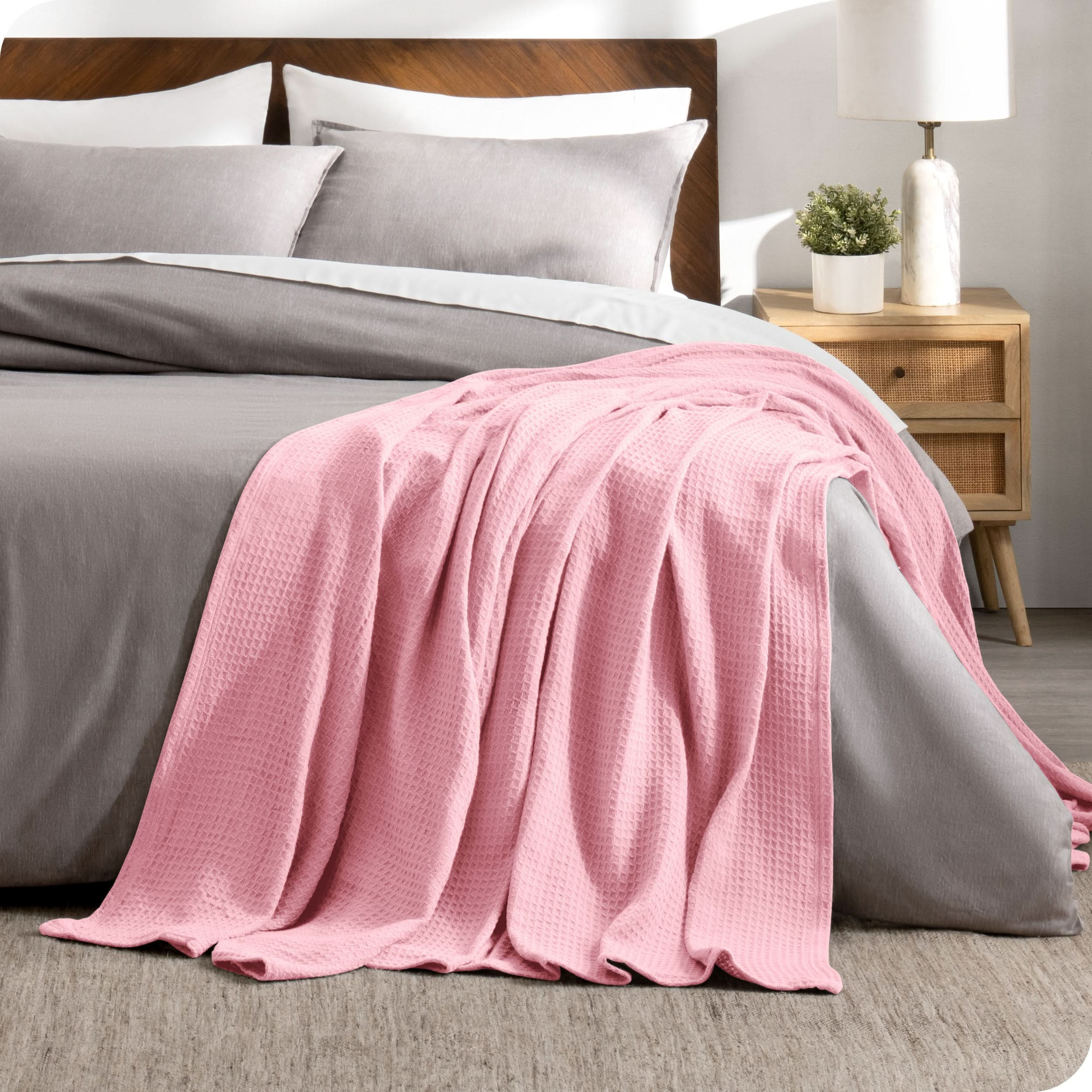 A cotton waffle blanket is on the corner of a bed. It is hanging down the side and end of the bed.