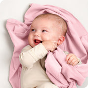 A baby lying on a receiving blanket. She has her thumb in her mouth.