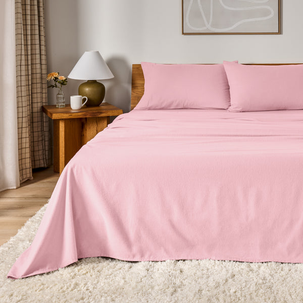 A bed dressed in flannel sheet set in a bedroom with a wooden headboard, bedside table and lamp