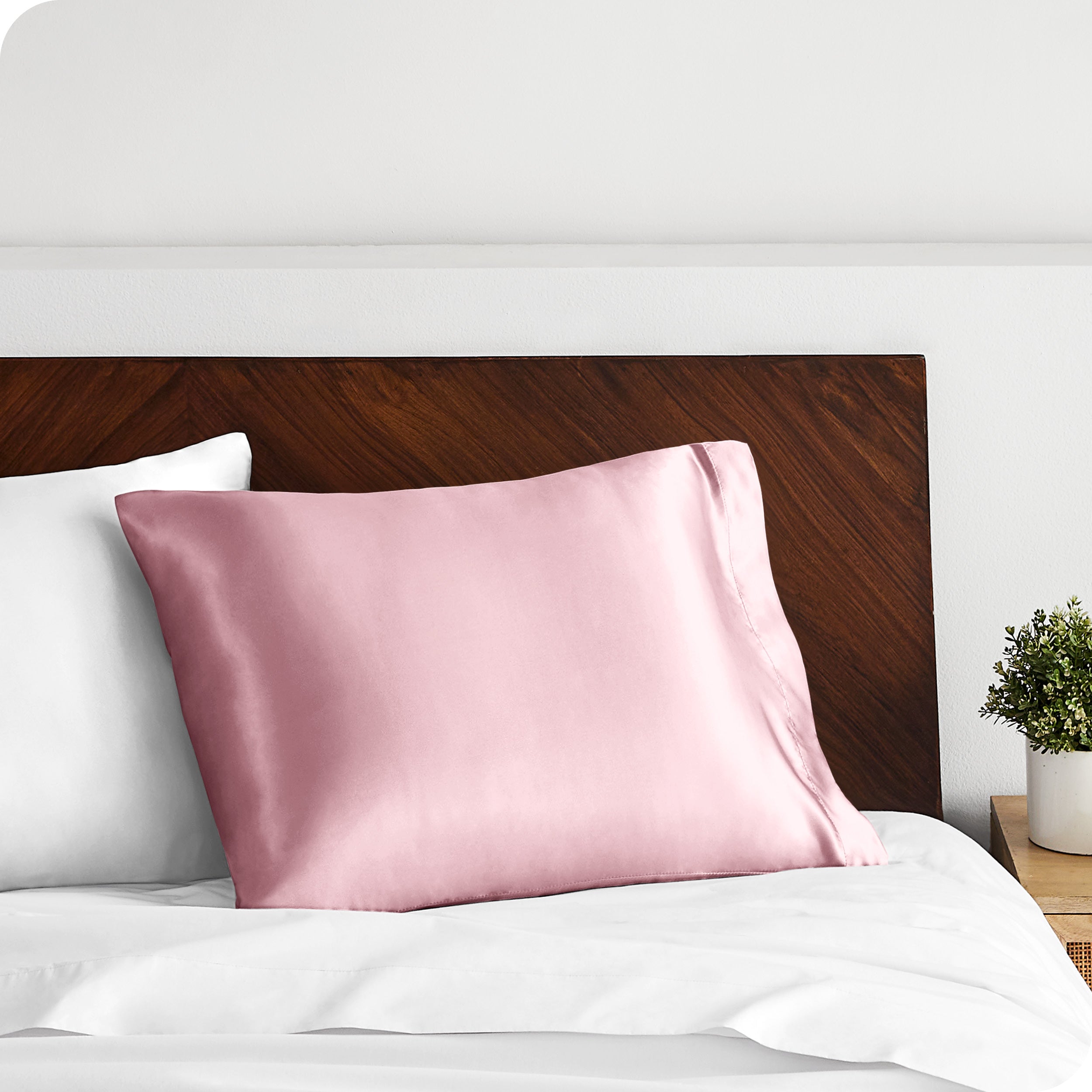 A pink silk pillowcase on a pillow resting on a headboard