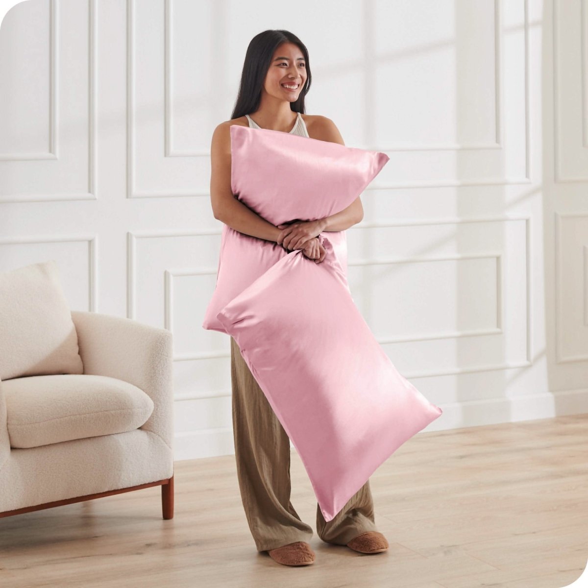 A woman standing while holding pillows with silk pillowcases on them