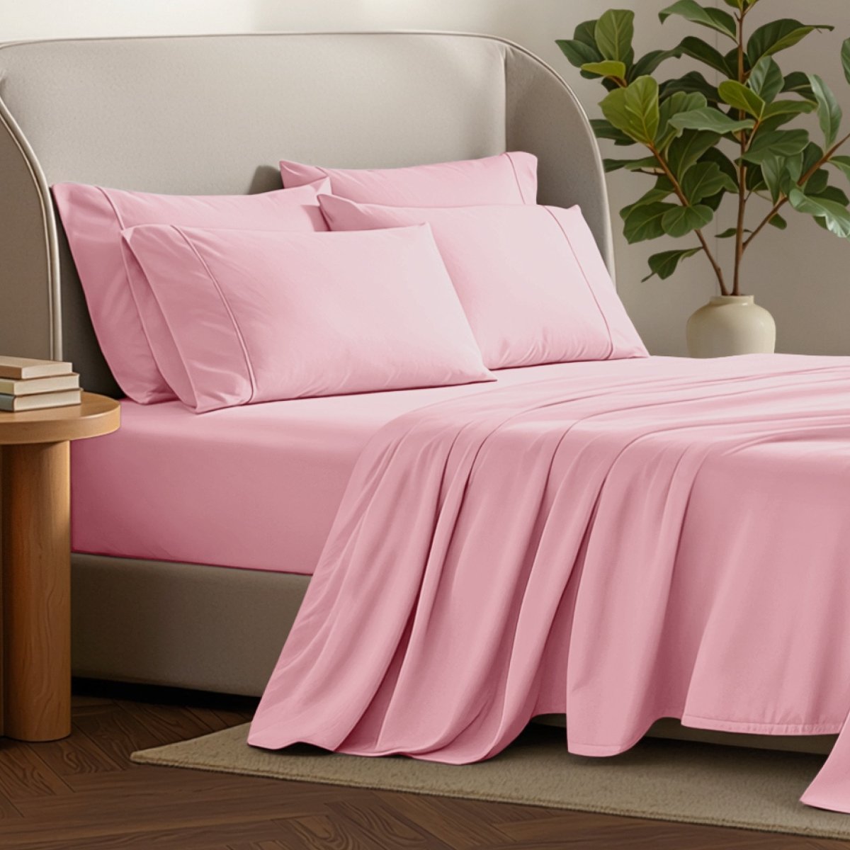 Bed sheets and pillows on a bed with a plant and side table in the background.