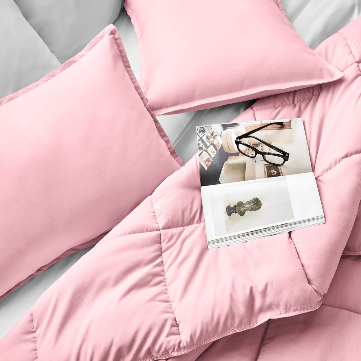 Comforter and pillows on a bed with a magazine and glasses.