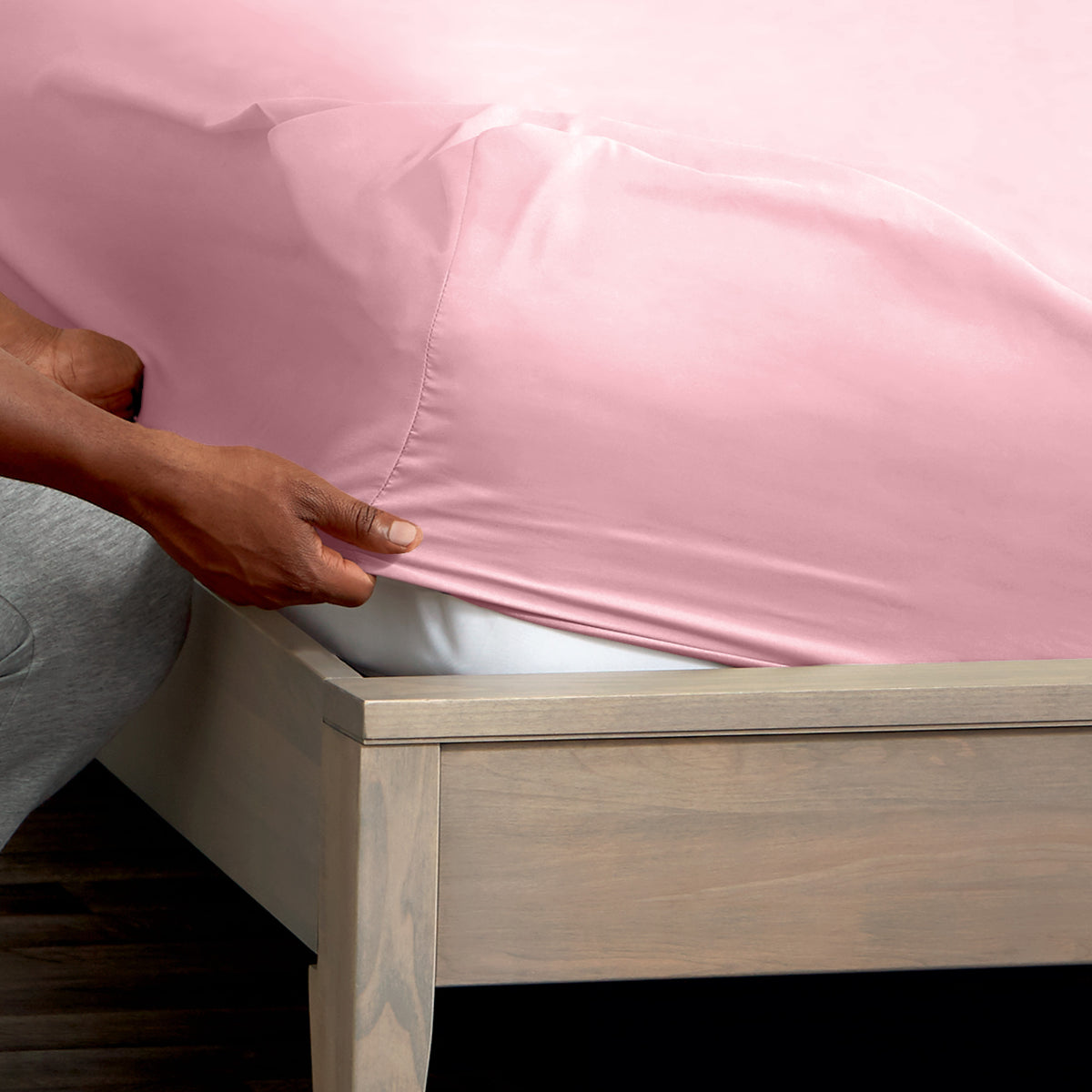 A man is putting a fitted sheet on a bed