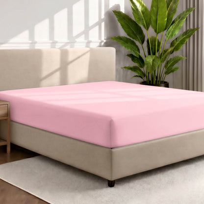 Bed with a fitted sheet in a room with a large plant and rug
