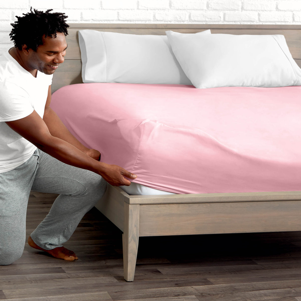 Man adjusting fitted sheet on a bed with white pillows.