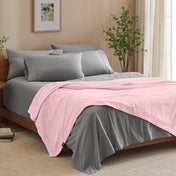 A bed made with grey sheets and a microplush blanket