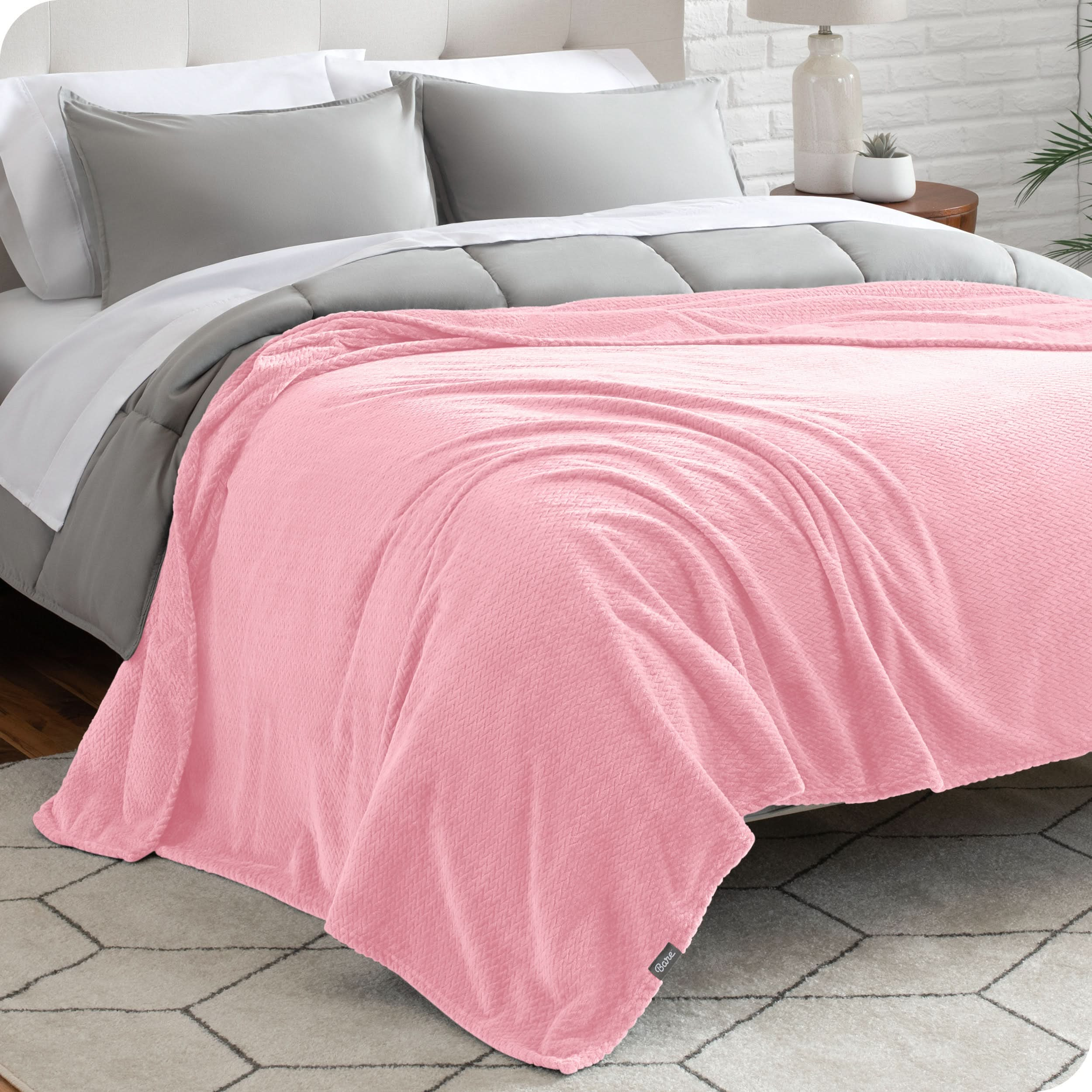 A textured microplush blanket is covering a bed, which has a comforter set on it.