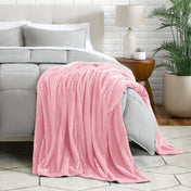 Blanket draped over a bed in a bedroom setting with a lamp and plant.