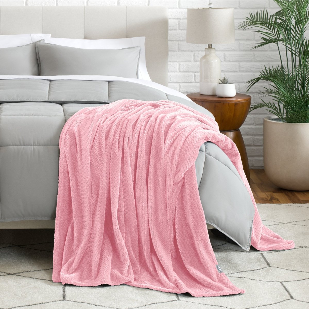 Blanket draped over a bed in a bedroom setting with a lamp and plant.