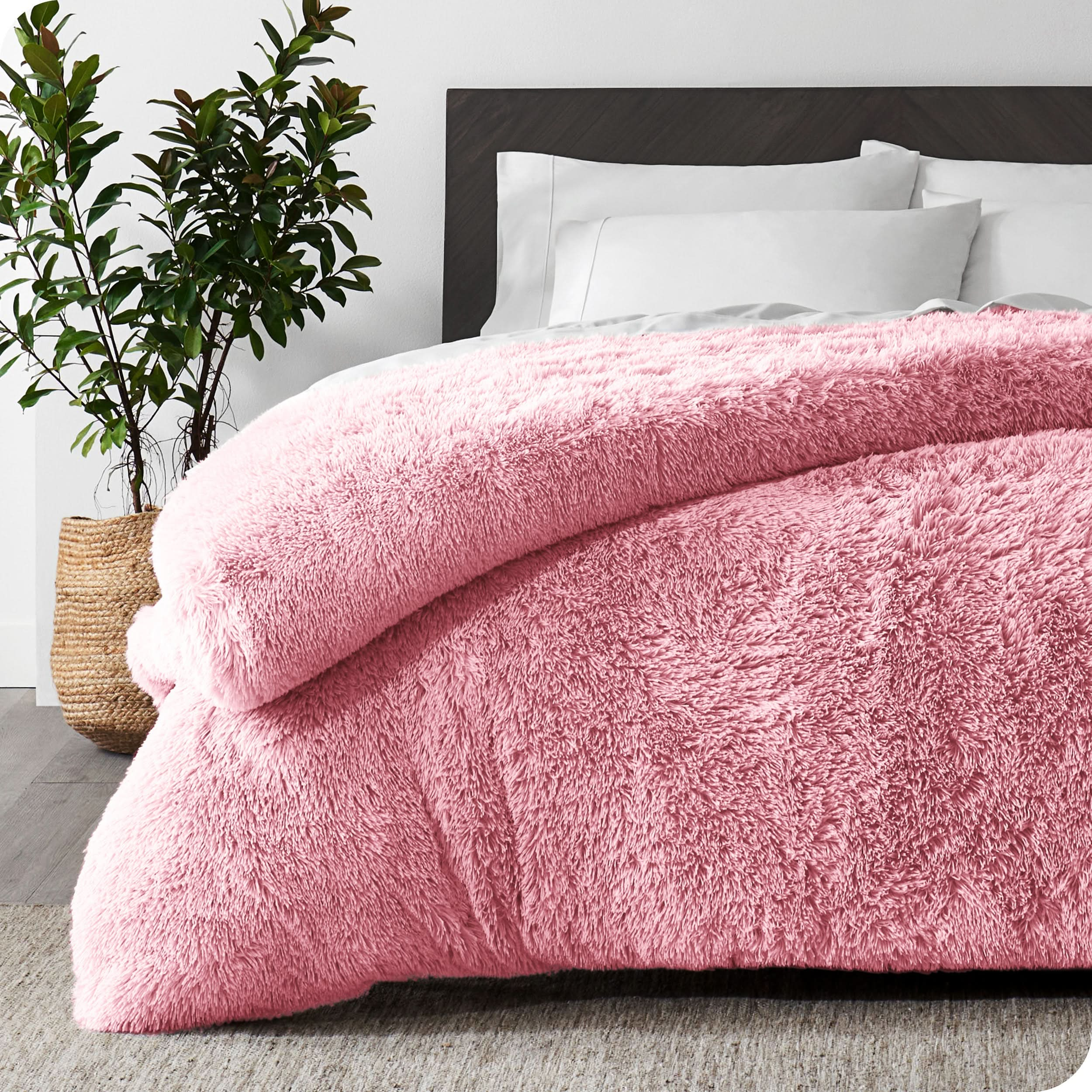 A pink shaggy duvet cover on a bed with white sheets and pillowcases. A large plant is next to the bed.