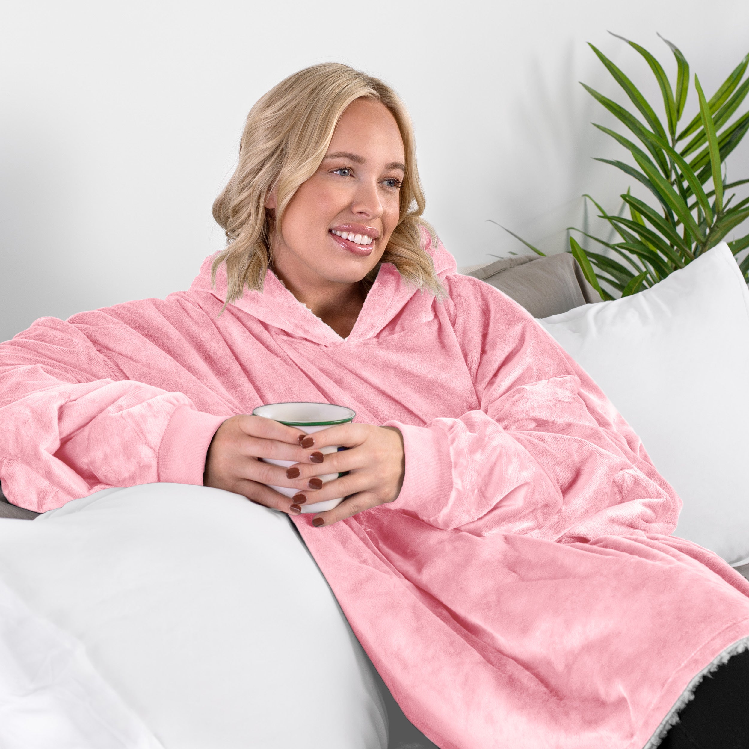 A woman sitting on a couch holding a mug wearing a sherpa blanket.
