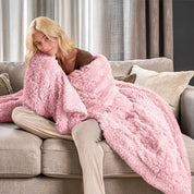A woman sitting on a couch with a shaggy blanket wrapped around her