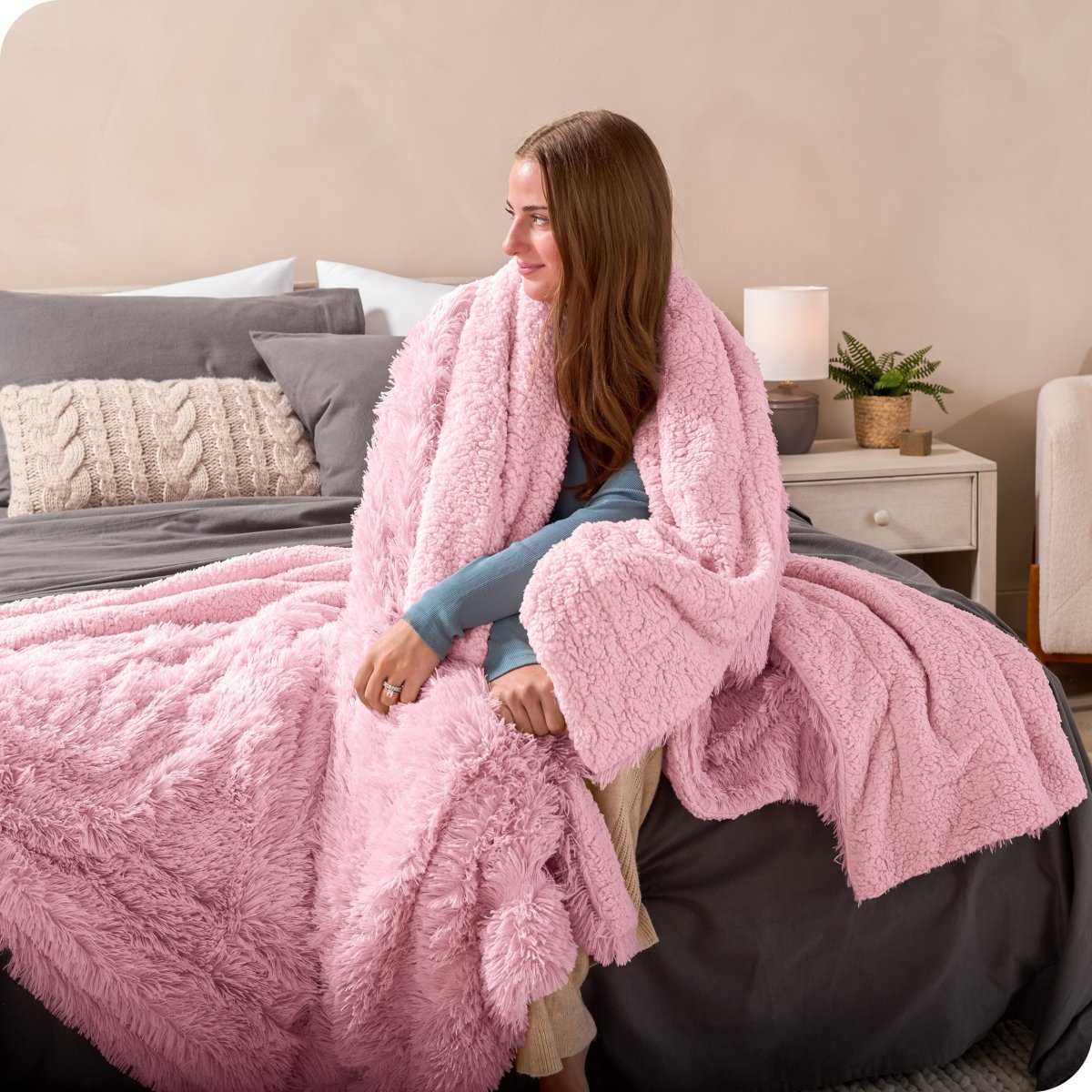 A woman sitting on the end of a bed with a shaggy blanket wrapped around her