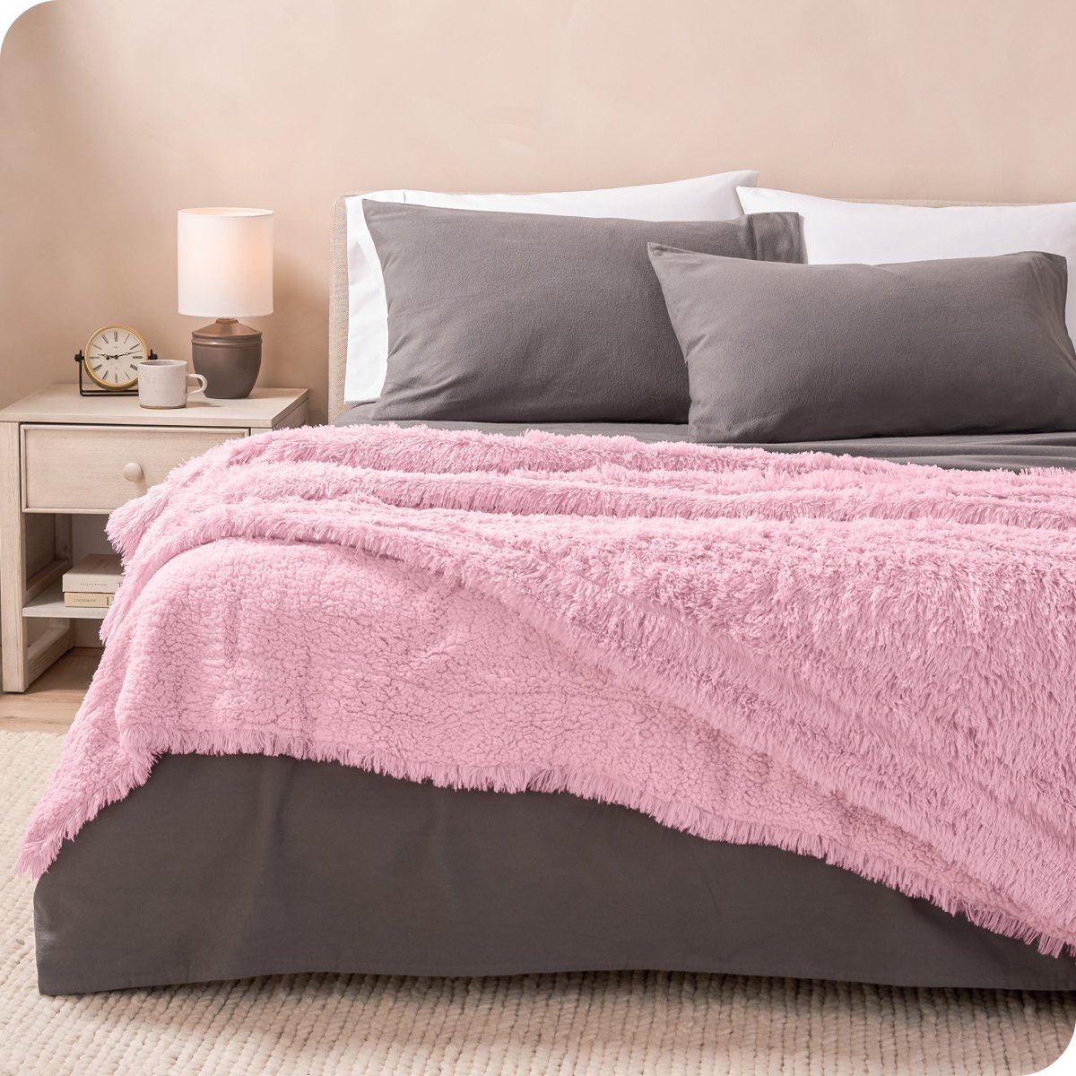 A woman sitting on the end of a bed with a shaggy blanket wrapped around her