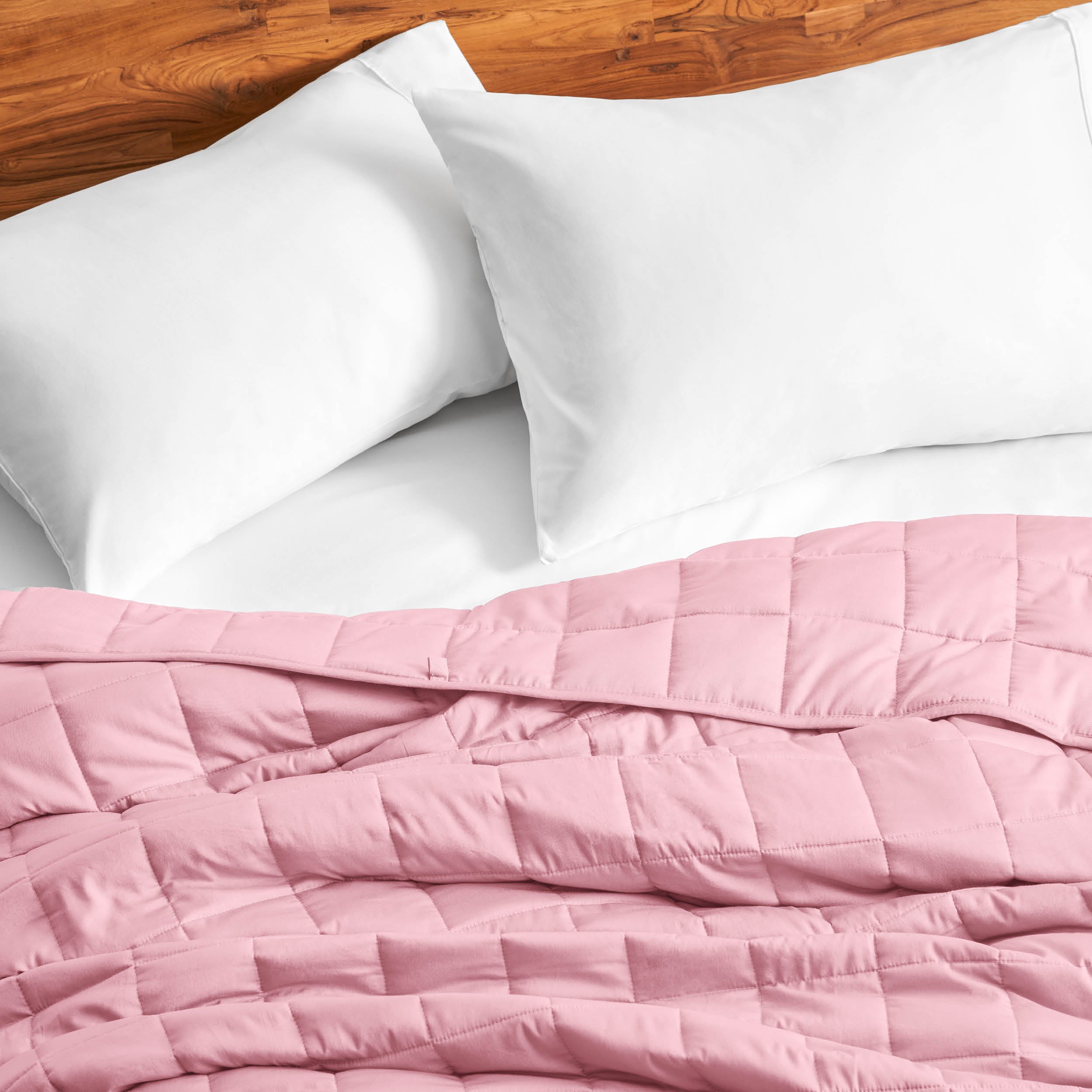 Cotton weighted blanket on a bed with white pillows against a wooden headboard.