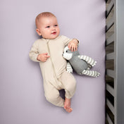 Baby in a beige onesie holding a gray and white striped toy while in a crib