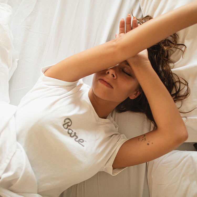 Person wearing a white t-shirt with 'Bare' text, lying on a bed.