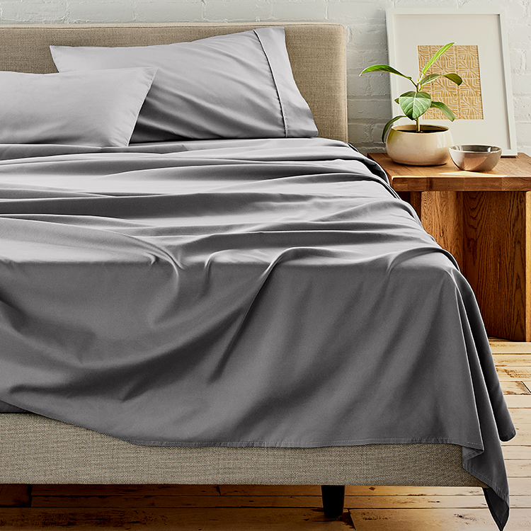 Gray bedding set on a bed with a wooden nightstand and plant in the background.