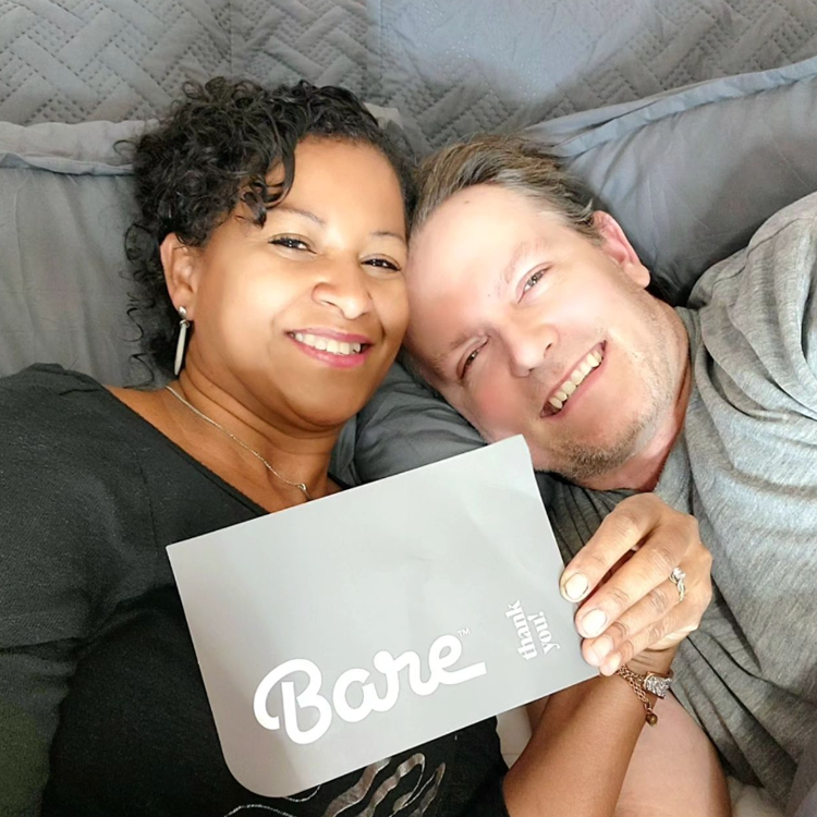 Two people lying on a bed holding a 'Bare' card.