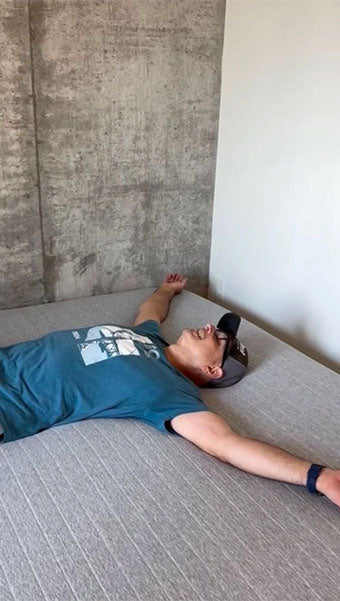 Man laying with arms out on new mattress
