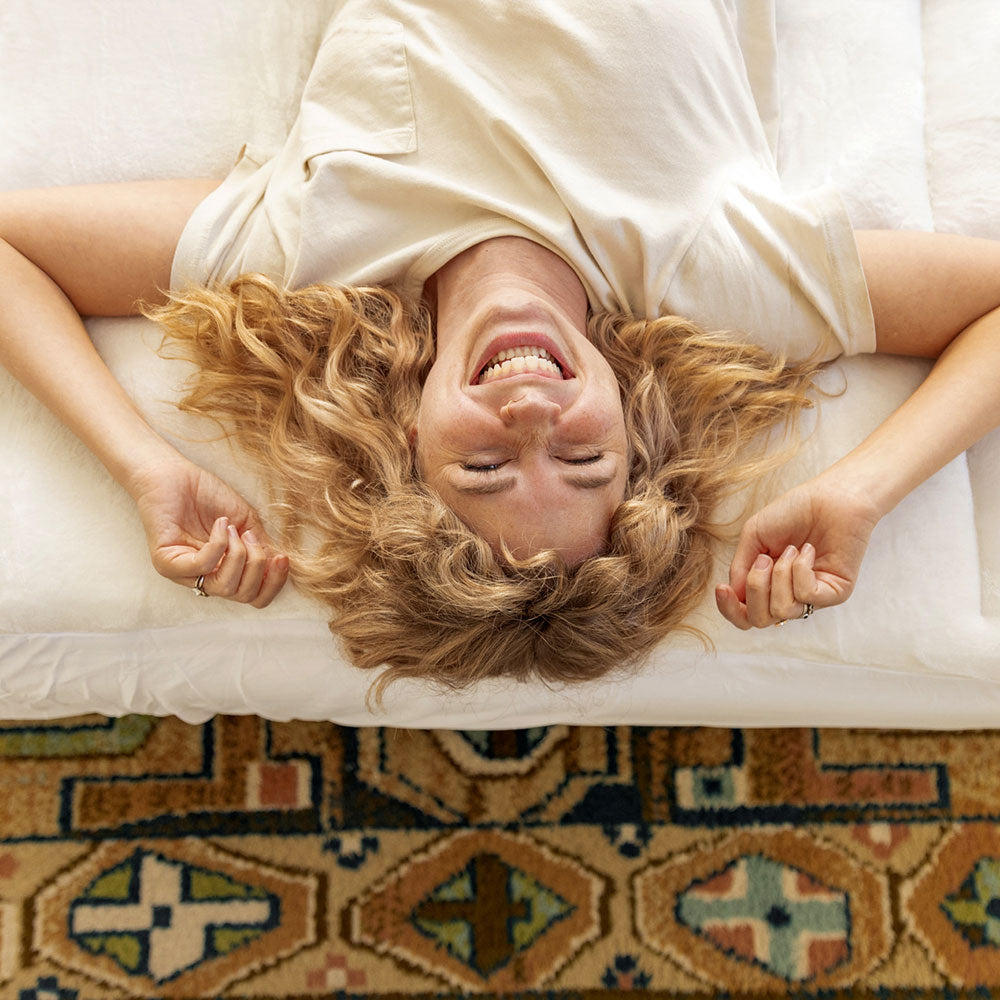 blonde lady laying on her back on a mattress topper