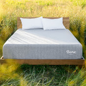 Gray mattress with white pillows on a wooden bed frame in a grassy field.
