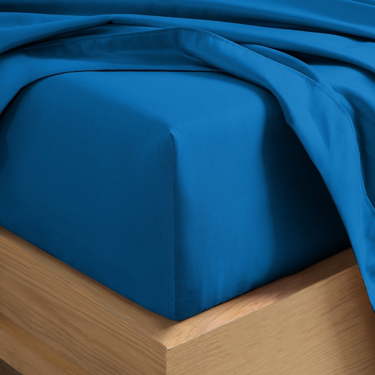 A close-up of a fitted sheet covering the corner of a bed frame, with matching top sheet draped over it.