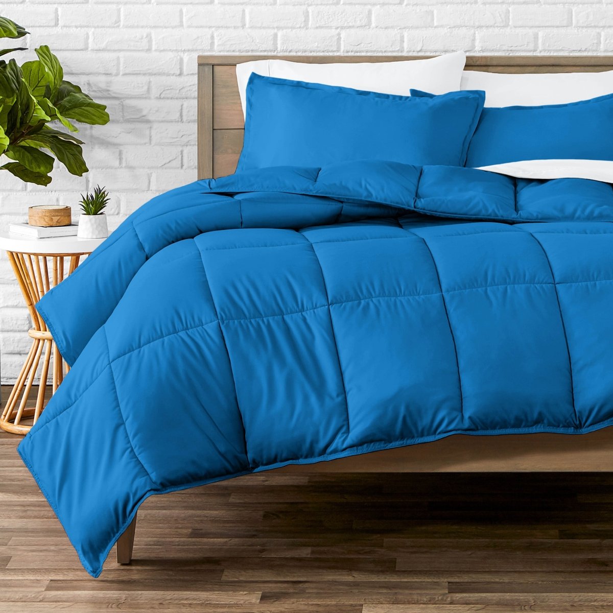 Comforter set on a bed with a white brick wall and plant in the background