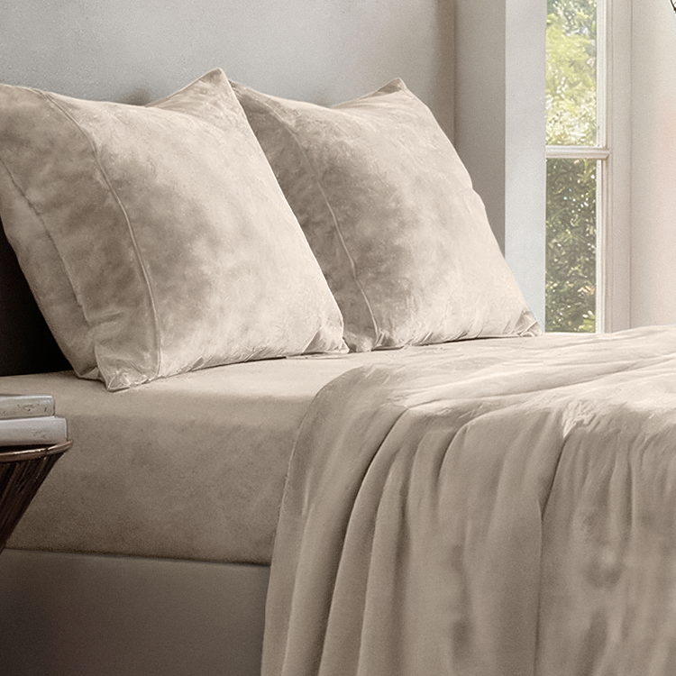 Beige bedding set with pillows on a bed in a room with a window.