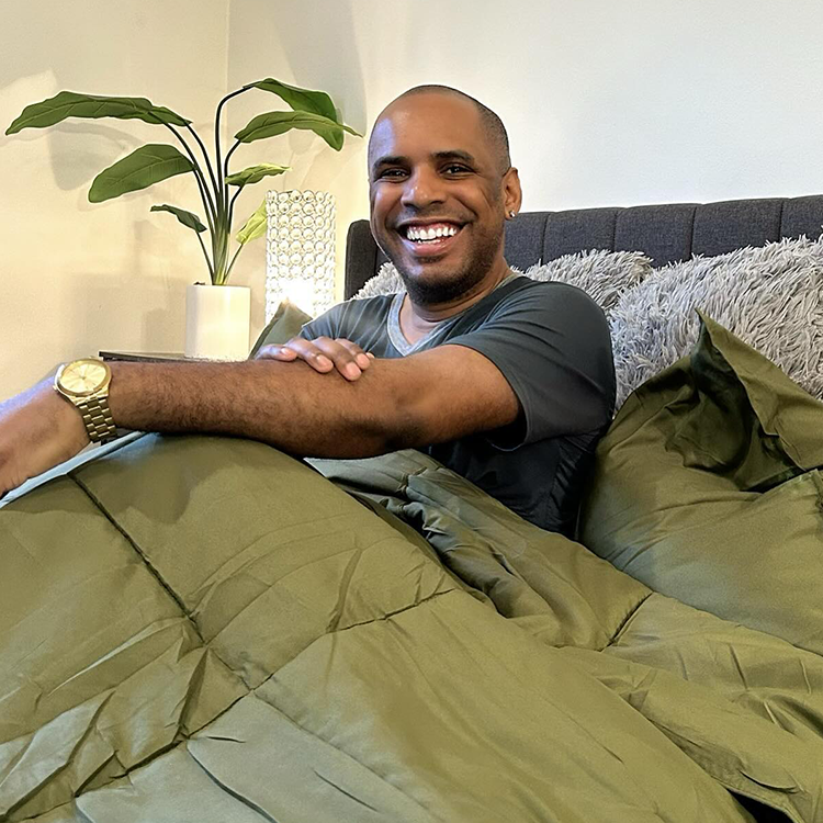 Man sitting on a bed with green bedding, smiling at the camera.